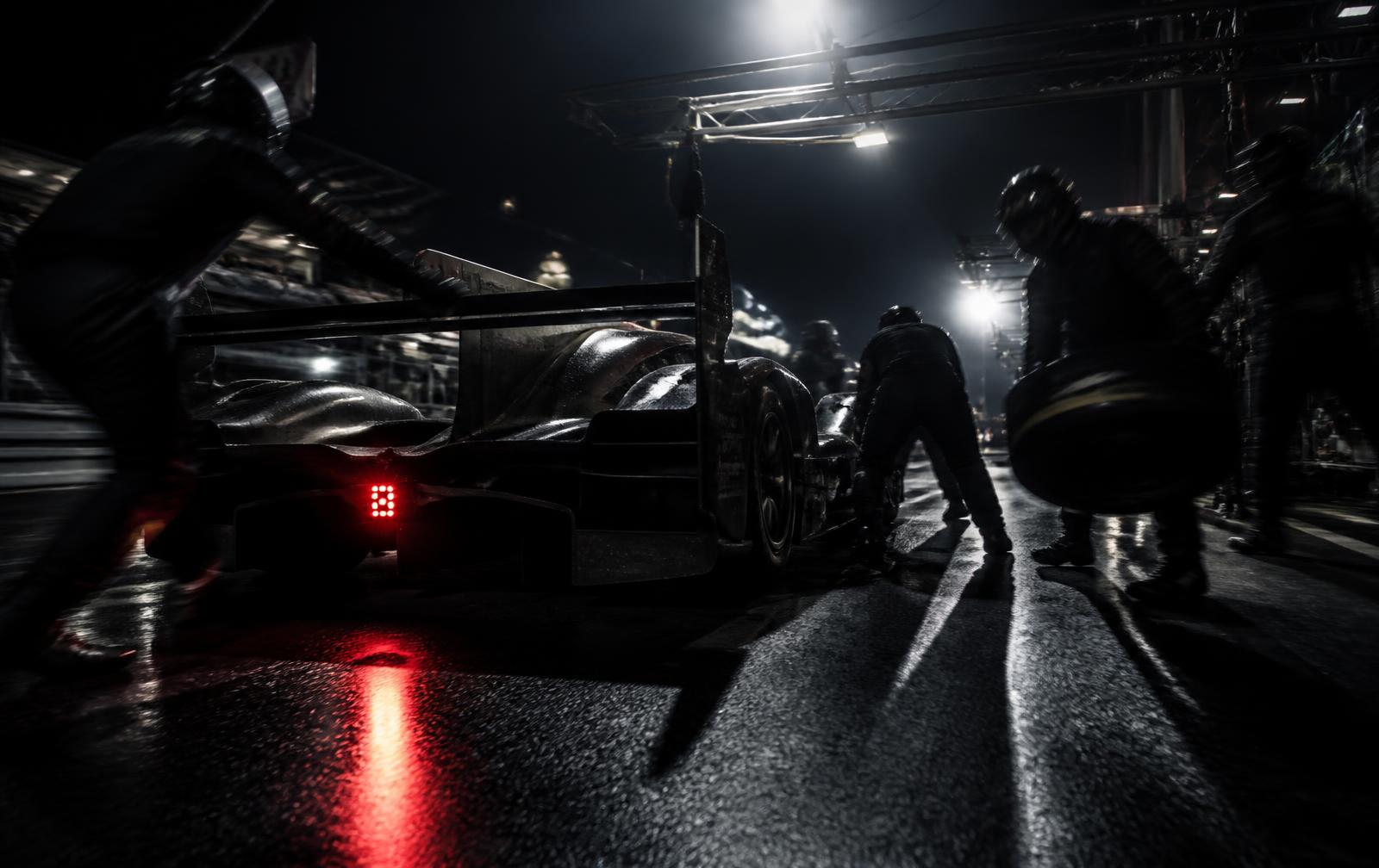 Pit crew working around a race car under night lights